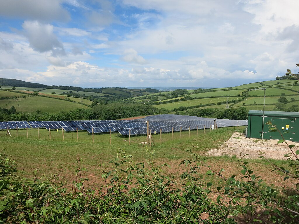 A series of green fields with hedges and a solar array in the center. There is a green shed in the right hand corner of the image and the sky is visible overhead.